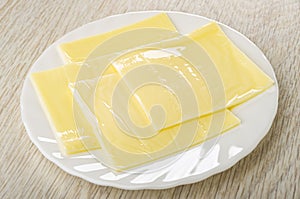 Slices of melted cheese in plate on wooden table