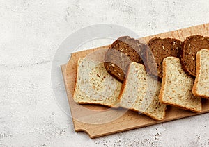 Slices of multigrain bread and rye bread on a wooden cutting board on a light gray background