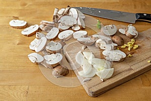 Slices of mushrooms, onion, chopped ginger and a kitchen knife on a wooden cutting board, cooking a healthy vegetarian dish, copy