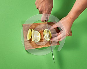 Slices of natural organic green lime, cutting by woman hands on a wooden cutting board on green.