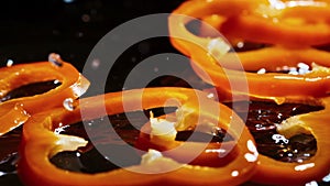 Slices of orandge bell pepper fall down on brown wooden board with water drops