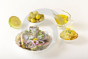 Slices of pickled herring with red onion, fermented cucumber, fried potatoes, olives and lime on a l