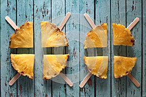 Slices of pineapple on popsickle sticks on blue wooden background flat lay