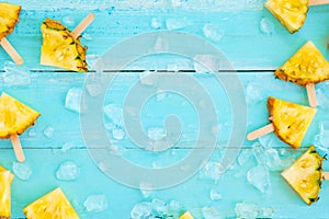 Slices pineapple popsicle sticks with ice on wood plank blue color.