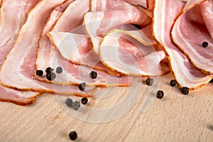 Slices of pink bacon with black peppercorn on wooden board