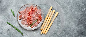 Slices of prosciutto di parma or jamon serrano in a plate and breadsticks. Gray concrete background. Top view, flat lay