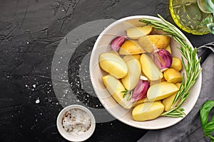 Slices of raw fresh potatoes before cooking with basil, rosemary, butter, garlic and salt for baking in country style