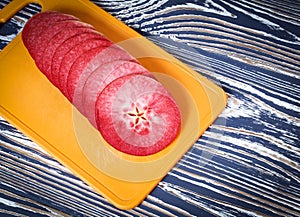 Slices of red apple are on the yellow cutting board