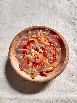 Slices red chilli in wooden bowl.