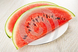 Slices of red watermelon in white plate on wooden table