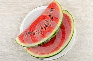 Slices of red watermelon in white plate on wooden table. Top view