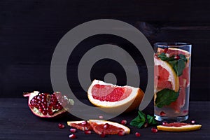 Slices of ripe grapefruit and pomegranate on black background with glass of red cocktail. detox water. diet healthy eating and wei