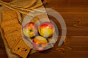 Slices of rye bread, three apples, ears of wheat on sacking, wooden table