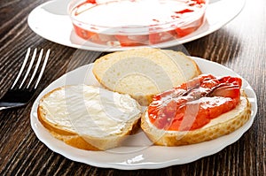 Slices of salted pink salmon in jar on background, fork, plate with sandwiches on wooden table