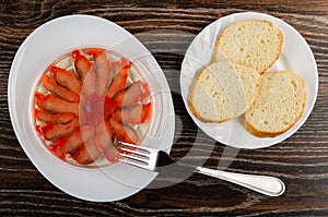 Slices of salted pink salmon in jar on plate, fork, pieces of bread in plate on wooden table. Top view