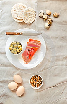 Slices of Salted Raw fish fillet with olive, quail eggs and nuts on white plate.Top view. Selection of good fat sources - healthy