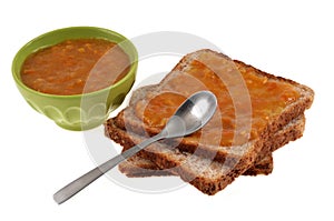 Slices of sandwich bread with clemantine jam and a spoon and a ramekin of jam on a white background