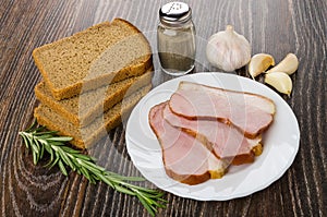 Slices of smoked gammon in plate, rye bread, pepper, garlic