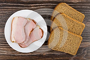 Slices of smoked gammon in plate, rye bread on table