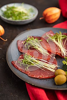 Slices of smoked salted meat with cilantro microgreen on black. Side view, selective focus