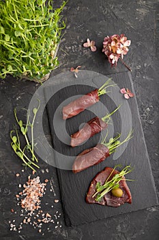 Slices of smoked salted meat with green pea microgreen on black. Top view, close up