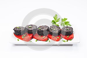 Slices of Spanish black pudding on piquillo peppers in white plate on white background. Spanish tapas