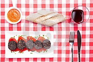 Slices of Spanish black pudding on piquillo peppers in white plate on a red checkered tablecloth . Spanish tapas