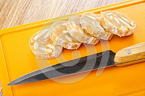Slices of sweet sausage, kniofe on plastic cutting board on wooden table