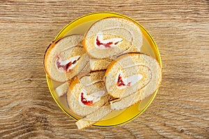 Slices of swiss roll with cream and jam in saucer on wooden table. Top view