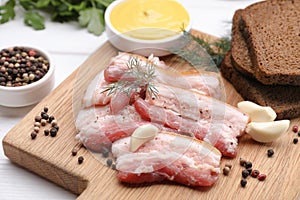 Slices of tasty pork fatback with garlic, rye bread and sauce on wooden board, closeup