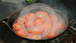 Slices of tomates is frying on frying pan with oil in grill, top view.