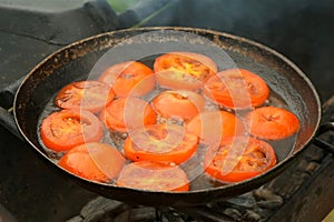 Slices of tomates is frying on frying pan with oil in grill, top view.