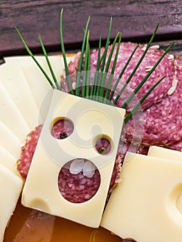 Slices of various cheeses, sausages and meat are arranged on a plate. The art of making a slice of cheese with holes looks like a