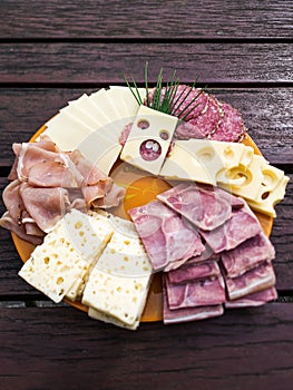 Slices of various cheeses, sausages and meat are arranged on a plate. The art of making a slice of cheese with holes looks like a