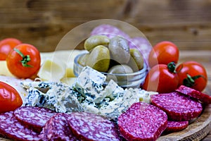Slices of various types of cheese and dry smoked salami sausage on wooden background. Traditional italian antipasto platter