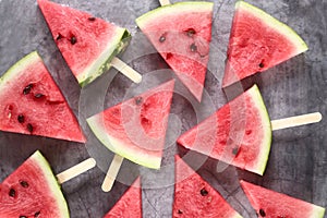 Slices of water-melon on popsickle stick on gray background flat lay