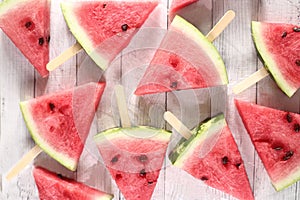Slices of water-melon on popsickle stick on white wooden background flat lay