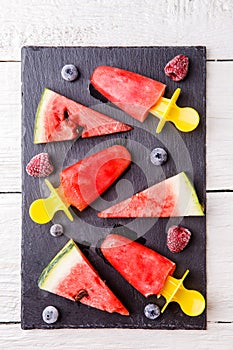 Slices of watermelon, fruit ice, frozen blueberries, raspberries on black board