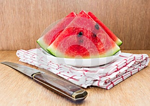 Slices of watermelon and a knife on a plate on a wooden background