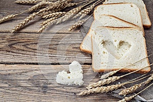 Slices of white bread and wheat ears on sacking on a wooden tabl