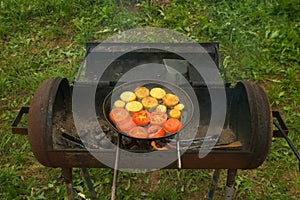 Slices of zucchini and tomatoes are frying on frying pan with oil in chargrill.