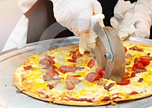 Slicing Fresh Made Italian Pizza, Closeup hand of chef cutting pizza in kitchen
