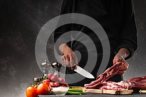 Slicing fresh meat, pork ribs on a background of fresh vegetables and a gray wall with space