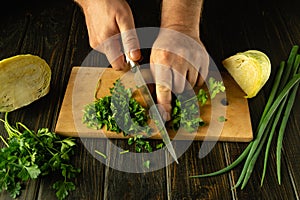 Slicing fresh parsley with a knife in the hands of a cook on a cutting board. Low key concept of preparing vegetable salad