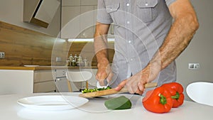 Slicing green bell pepper on wooden cutting board. Male hand cuts capsicum with knife. Man is cutting the sweet