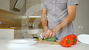 Slicing green bell pepper on wooden cutting board. Male hand cuts capsicum with knife. Man is cutting the sweet