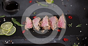 Slicing grilled fried tuna steak covered with sesame seeds on a black stone serving board