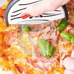 Slicing ham pizza with roller knife from above photo