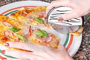 Slicing ham pizza with roller knife photo