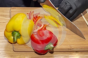 Slicing paprika cook. cooking healthy food diet healthy food. wooden cutting board on wooden table, chef hands in black rubber glo